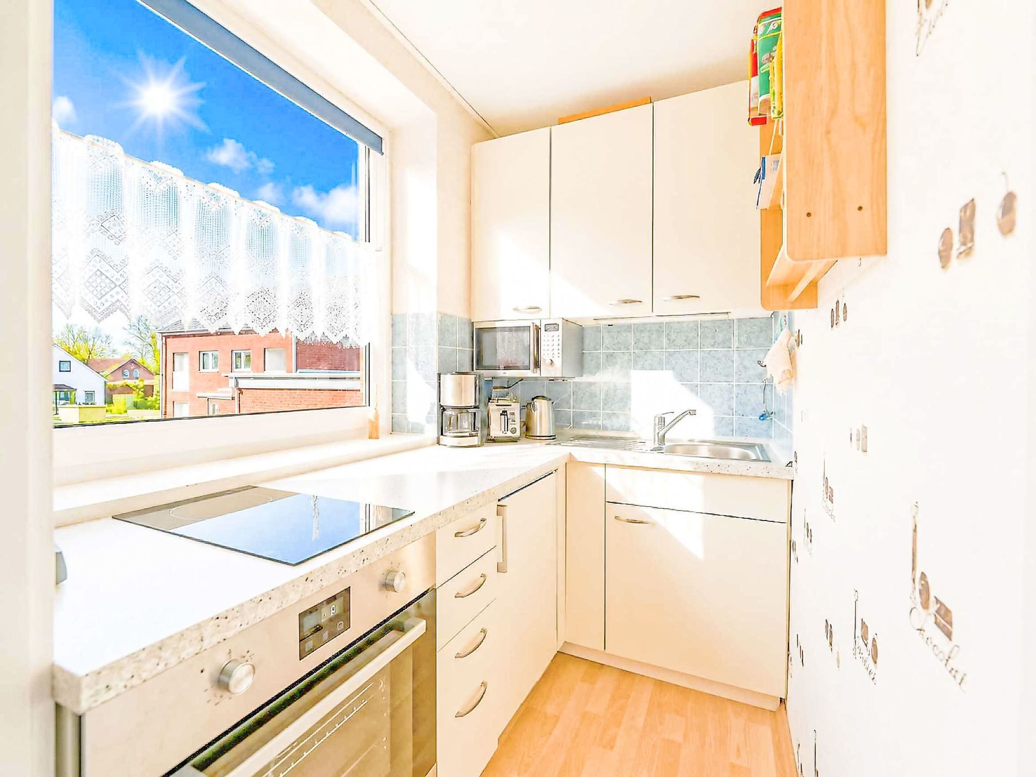 Uma cozinha moderna com armários brancos, forno embutido, micro-ondas e janela com vista para edifícios.