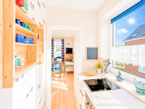 A kitchen with wooden cabinets, a stove, and a window with a view of a house. - Meeresrauschen by Interhome (Burhave)