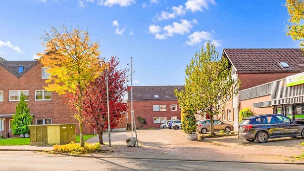 Rua residencial com casas de tijolo, carros estacionados e árvores com folhagem outonal.