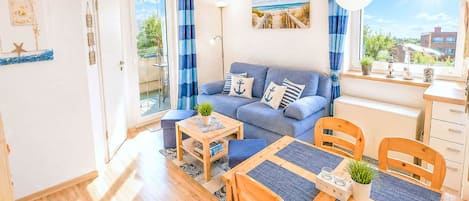 A cozy living room with a sofa, a dining table with chairs, a small side table, and a view of the outdoors through a window.