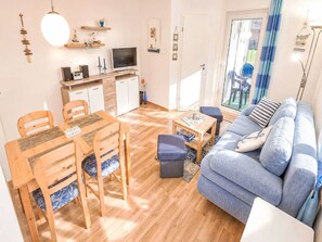 Ein gemütliches Wohnzimmer mit Sofa, Esstisch, Stühlen, Fernseher und einer Küchenzeile mit Schränken und Arbeitsplatte.