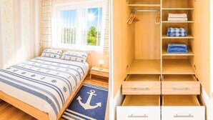 Um quarto com uma cama, uma mesa de cabeceira, uma janela com cortinas e um guarda-roupa de madeira com várias prateleiras e gavetas.