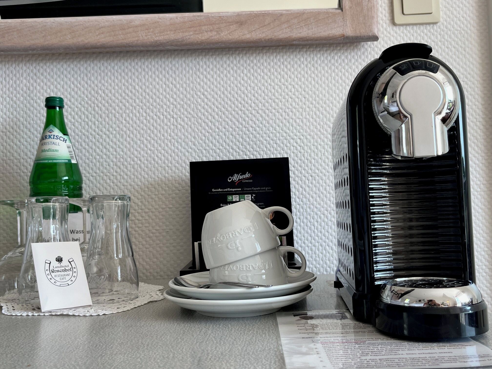Ein gedeckter Tisch mit Flasche, Gläsern, einer Kaffeemaschine und einer Speisekarte.