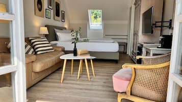 A hotel room with a bed, a sofa, a small table, a chair, a TV, and a window.