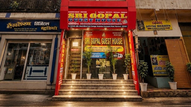 Un edificio con fachada roja y un letrero que dice 'Sri Gopal Guest House', con una escalera que lleva a la entrada.