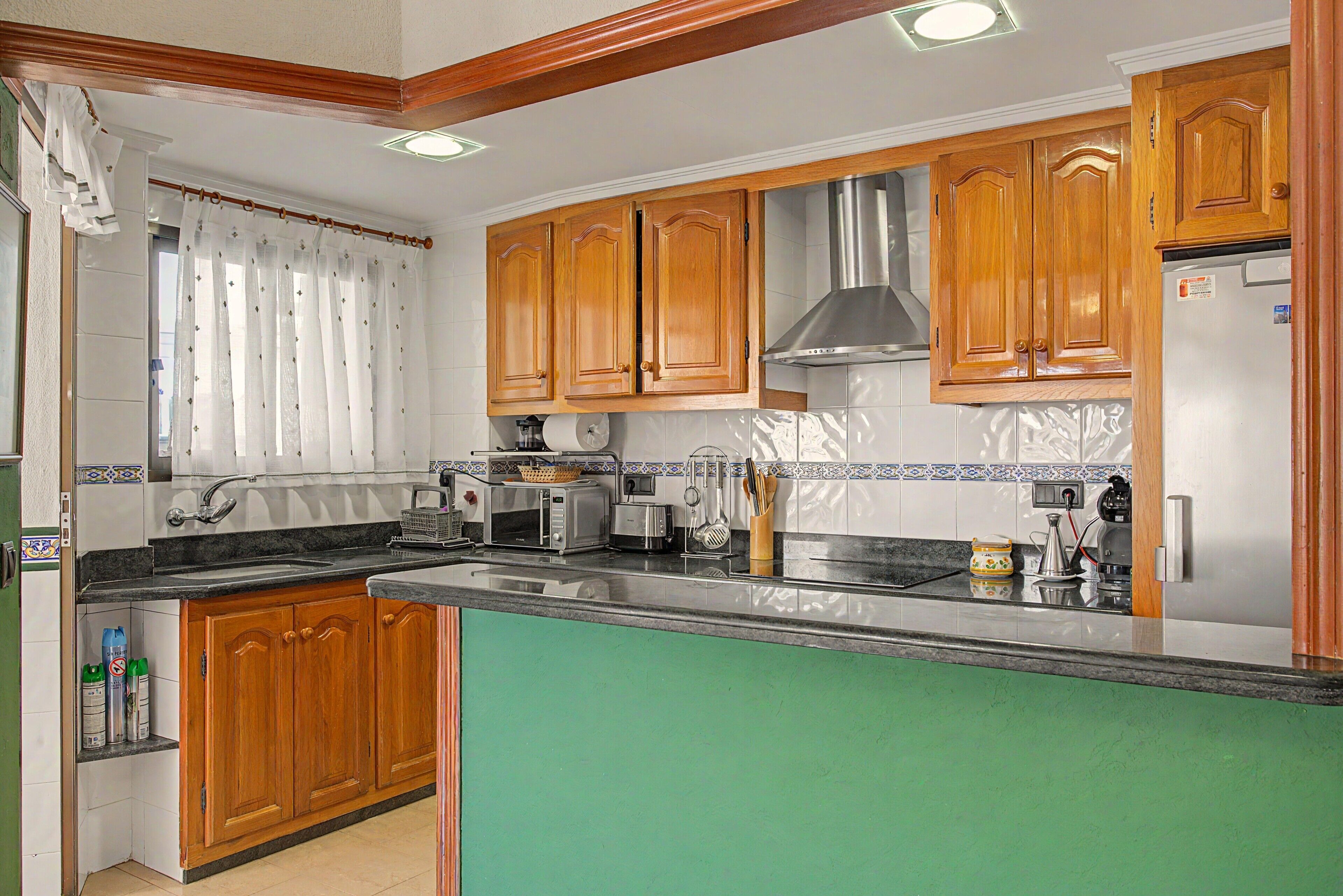 Cocina con armarios de madera, refrigerador de acero inoxidable, microondas y pileta.