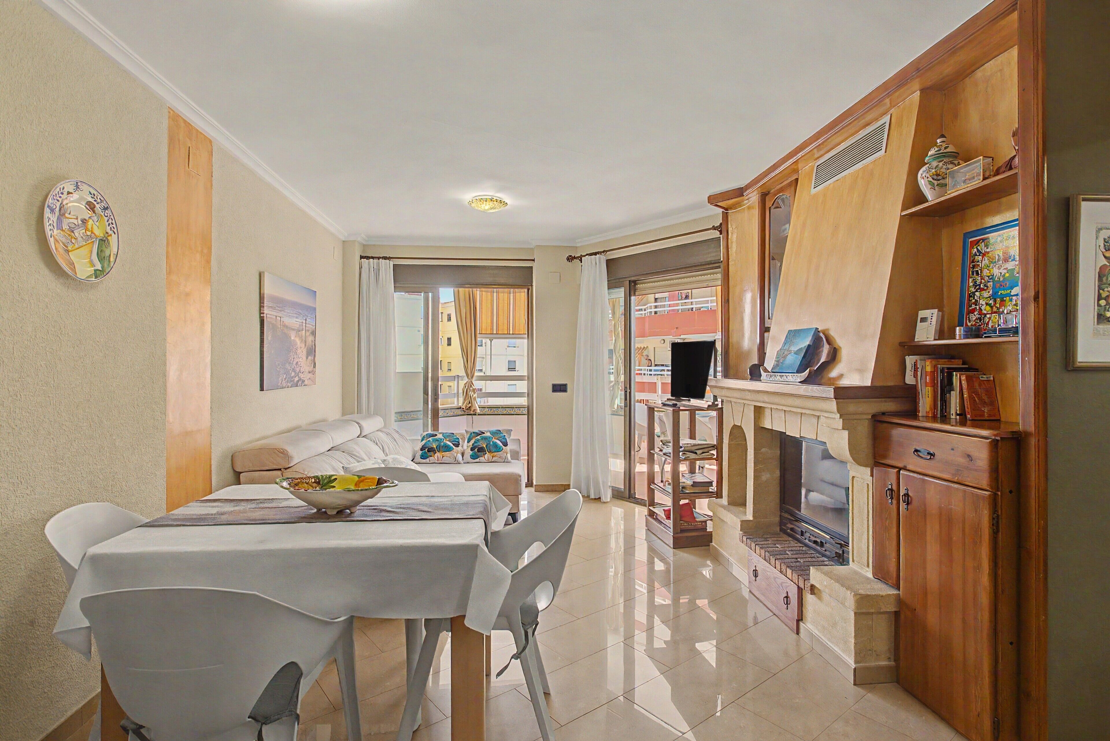 A dining area with a table set for two, a sofa, and a view through a glass door to the outside.