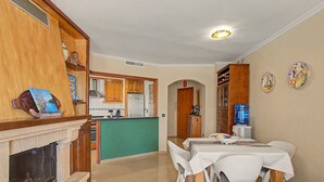 A dining area with a table and chairs, a kitchen in the background, and a water dispenser on the wall. - Casa Dolo · Beachfront Apartment with Pool, Elevator, and WiFi (Tavernes de la Valldigna)