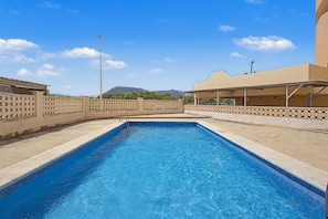 Une piscine rectangulaire à l’eau d’un bleu limpide, entourée d’une terrasse carrelée de couleur beige et d’une clôture décorative.