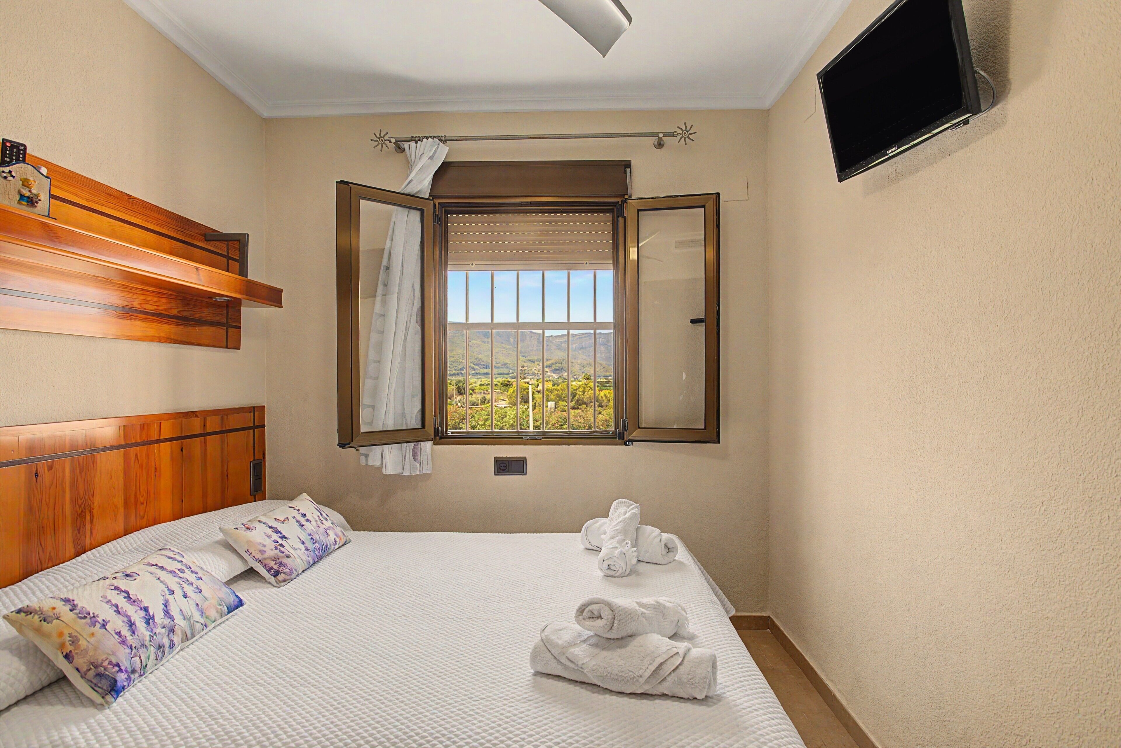 Een hotelkamer met een bed, een raam met uitzicht, een flatscreen televisie en een houten hoofdeinde.