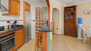 A kitchen with wooden cabinets, a stainless steel refrigerator, a coffee maker, and a water dispenser. - Casa Dolo · Beachfront Apartment with Pool, Elevator, and WiFi (Tavernes de la Valldigna)