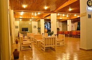 Une pièce spacieuse dotée d’un plancher et d’un plafond en bois, aménagée avec de nombreux fauteuils et tables, et un téléviseur fixé au mur.