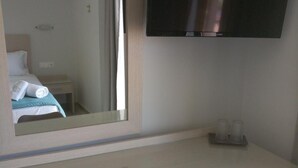 Ein Hotelzimmer mit einem Bett, einem Schreibtisch mit Spiegel, einem Fernseher und einem Kühlschrank.