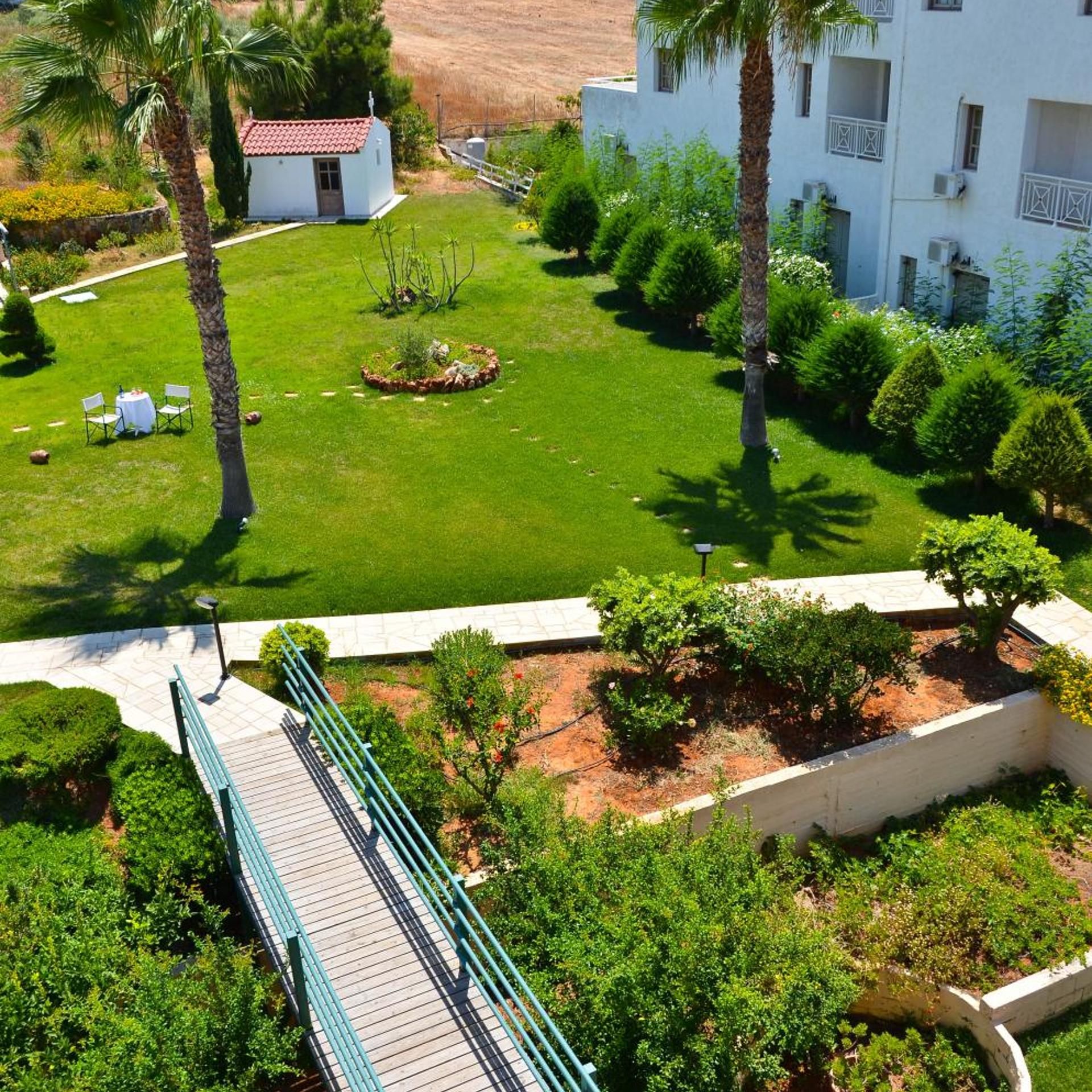 Un jardín ajardinado con un edificio blanco, palmeras y un puente.