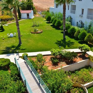 A landscaped garden with a white building, palm trees, and a bridge. - Niko Elen Hotel (Hersonissos)