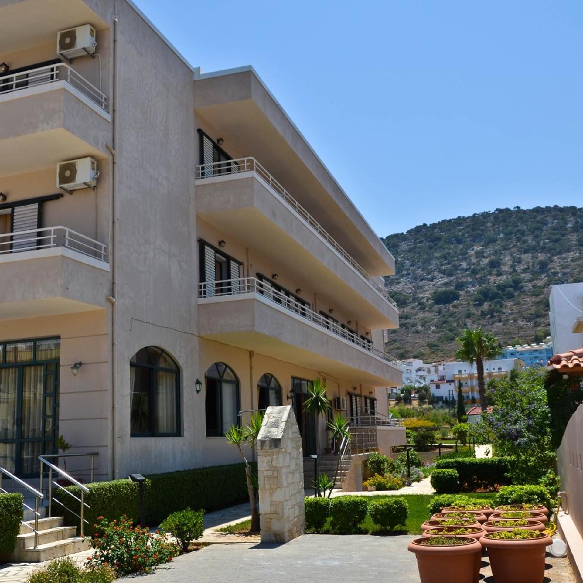 A multi-story building with balconies, a stone base, and a view of a hilly landscape.