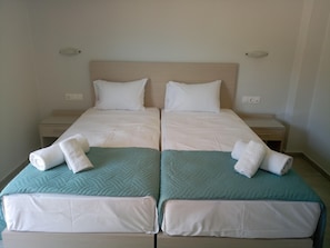 A double room with two beds, each with a pillow, a nightstand, and a folded towel. - Niko Elen Hotel (Hersonissos)