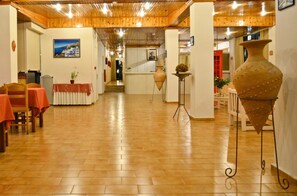 A hotel corridor with wooden flooring, tables with red tablecloths, and a large vase on a stand. - Niko Elen Hotel (Hersonissos)
