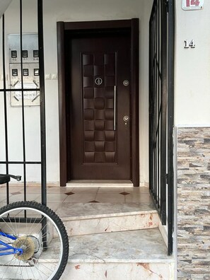 A brown door with a keypad lock, a bicycle parked to the left, and a stone wall to the right. - Özler Apart Pansiyon (Edremit)