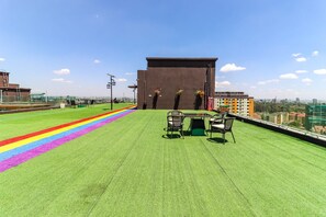 Eine Dachterrasse mit Kunstrasen, einem Tisch und Stühlen sowie Blick auf die Stadtlandschaft.