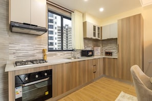Cozinha moderna com fogão a gás, forno e micro-ondas. Há uma janela com cortinas, e a cozinha possui armários de madeira e painel de azulejos.