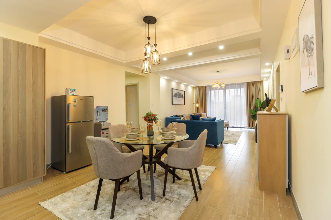 Una cocina moderna con refrigerador empotrado, una mesa de comedor con sillas y un sofá azul al fondo.