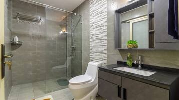Un baño moderno con ducha envuelta en vidrio, inodoro blanco, tocador oscuro con lavamanos y espejo sobre el tocador.