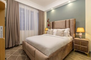 Ein Hotelzimmer mit einem großen Bett, zwei Nachttischlampen, einem Nachttisch und einem Fenster mit Vorhängen.