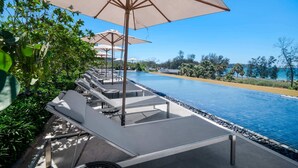 A poolside area with lounge chairs and umbrellas, a clear blue pool, and a view of the sea. - Seashore Residences, Three-Bedroom 3B Deluxe (Thalang)