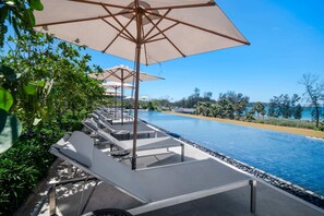 A poolside area with lounge chairs and umbrellas, a clear blue pool, and a view of the sea. - Seashore Residences, Three-Bedroom 3B Deluxe (Thalang)