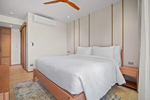 A modern bedroom with a wooden bed frame, a built-in bench, and a ceiling fan. - Seashore Residences, Three-Bedroom 3B Deluxe (Thalang)