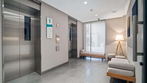 A modern elevator with a digital display, a wall-mounted sign, and a bench with a lamp. - Seashore Residences, Three-Bedroom 3B Deluxe (Thalang)
