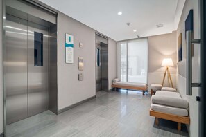 A modern elevator with a digital display, a wall-mounted sign, and a bench with a lamp. - Seashore Residences, Three-Bedroom 3B Deluxe (Thalang)