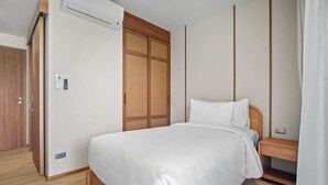 A bedroom with a bed, a wardrobe, a bedside table, and a wall-mounted air conditioner. - Seashore Residences, Three-Bedroom 3B Deluxe (Thalang)