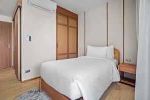 A bedroom with a bed, a wardrobe, a bedside table, and a wall-mounted air conditioner. - Seashore Residences, Three-Bedroom 3B Deluxe (Thalang)