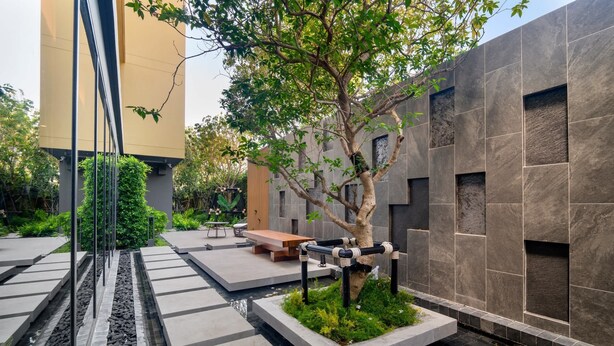 A modern outdoor area with a tree, benches, and a water feature. - Seashore Residences, Three-Bedroom 3B Deluxe (Thalang)