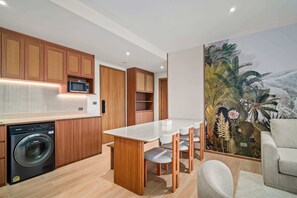 A modern kitchen with wooden cabinets, a built-in microwave, and a washing machine. - Seashore Residences, Three-Bedroom 3B Deluxe (Thalang)