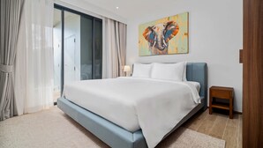 A modern bedroom with a large bed, a ceiling fan, a painting of an elephant, and a sliding glass door. - Seashore Residences, Three-Bedroom 3A Premium (Thalang)