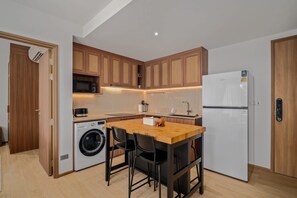 A compact kitchen with wooden cabinets, a microwave, a washing machine, and a refrigerator. - Seashore Residences, Three-Bedroom 3A Premium (Thalang)