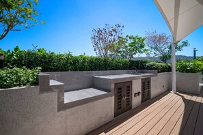 An outdoor kitchen area with a built-in sink and cabinets, surrounded by a wooden deck and a low concrete wall. - Seashore Residences, Three-Bedroom 3A Premium (Thalang)