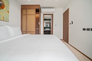 A hotel room with a large bed, a wardrobe with a woven panel, an air conditioning unit, and a view of the bathroom. - Seashore Residences, Three-Bedroom 3A Premium (Thalang)