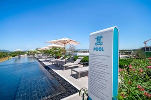 A pool area with lounge chairs and umbrellas, a sign indicating the pool, and a clear sky. - Seashore Residences, Three-Bedroom 3B Premium (Thalang)