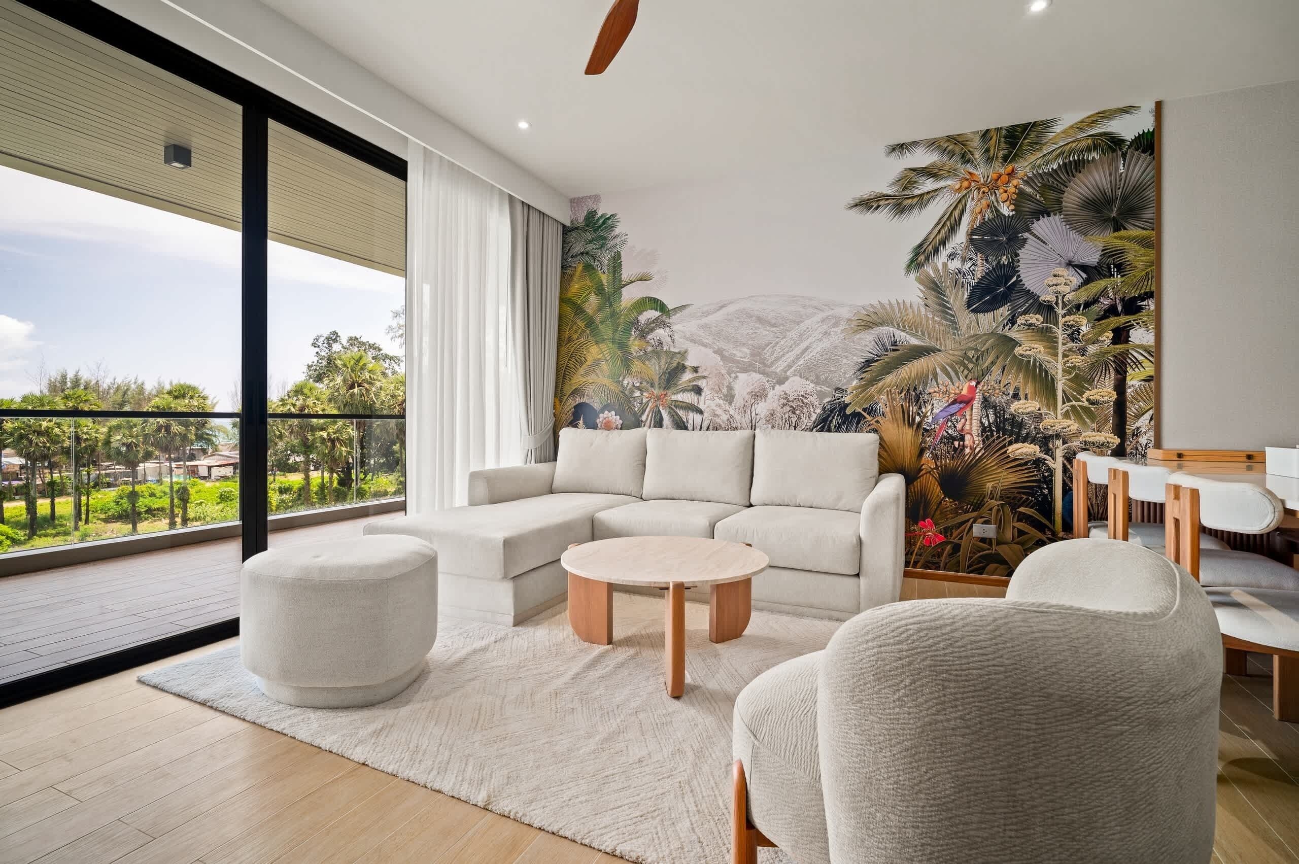 A modern living room with a large window, a sectional sofa, a round coffee table, and a tropical mural.