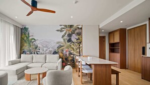 Een moderne woonkamer met een hoekbank, een ronde salontafel, een eettafel met stoelen, en een groot muurschildering van tropisch landschap.
