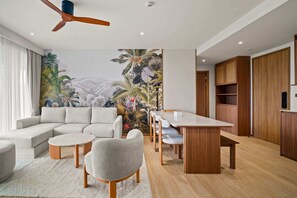 A modern living room with a sectional sofa, a round coffee table, a dining table with chairs, and a large mural of tropical scenery. - Seashore Residences, Three-Bedroom 3B Premium (Thalang)