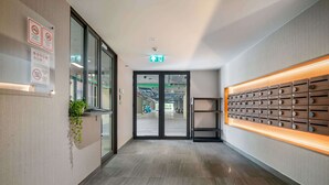 Een moderne hotelentree met een glazen deur, een aan de muur bevestigde plant en een houten paneelpresentatie.
