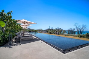 A pool with lounge chairs and umbrellas, surrounded by vegetation and a clear view of the sea. - Seashore Residences, Three-Bedroom 3A Deluxe (Thalang)