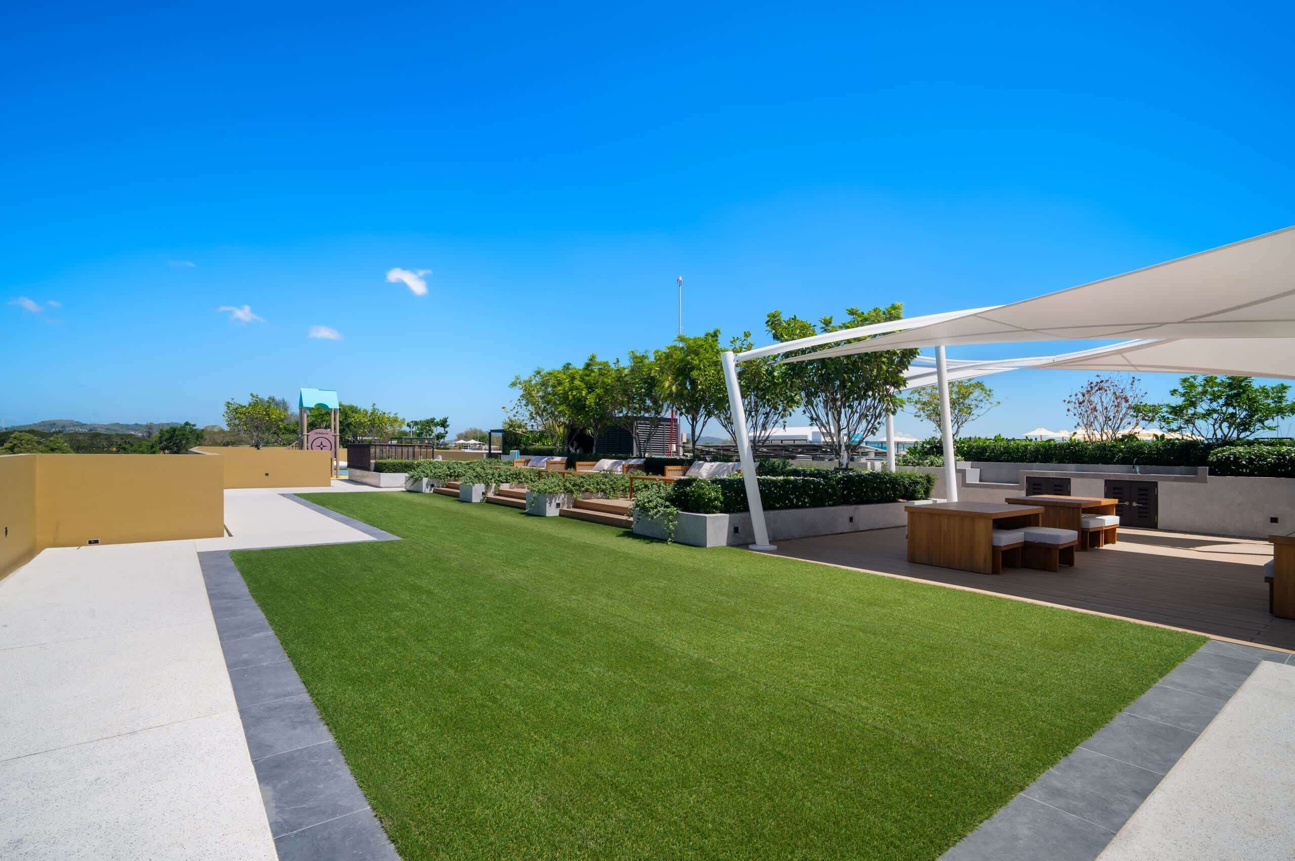 A rooftop garden with a lawn, seating area, and a white pergola.
