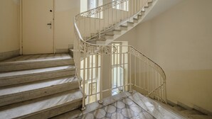 Un escalier en colimaçon avec une rampe en métal, menant à une porte dotée d’une petite fenêtre.