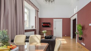 Un salon moderne avec une table à manger en verre, deux fauteuils, un canapé, un téléviseur fixé au mur et une plante en pot.